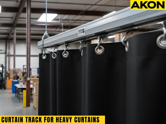 Heavy-duty curtain track supporting thick black industrial curtains in a warehouse setting