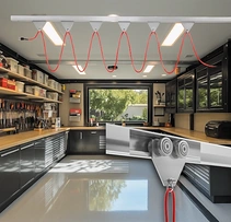 Red extension cords hanging in loops from trolleys on a ceiling track in a workshop