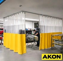 Welder working inside a shop enclosure of clear and yellow vinyl curtains on overhead track